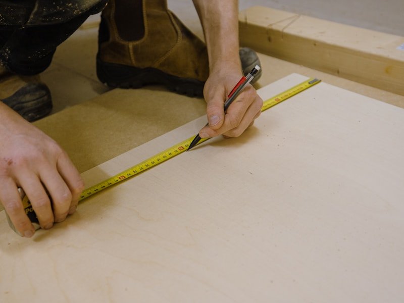 Craftsman marking a length of lumber with a yellow tape measure.