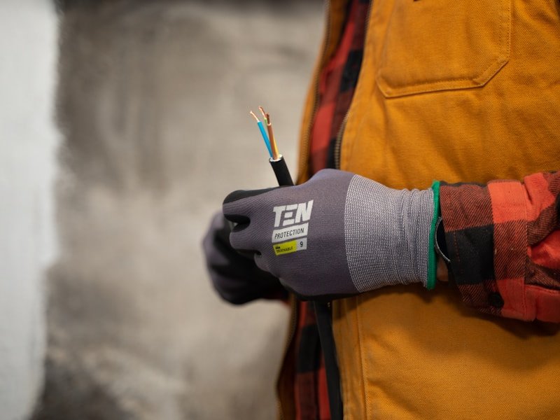 Gloved electrician's hand holding a stripped cable with exposed conductors.