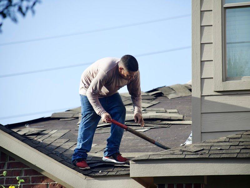 Contractor replacing damaged roof shingles and eaves trim.