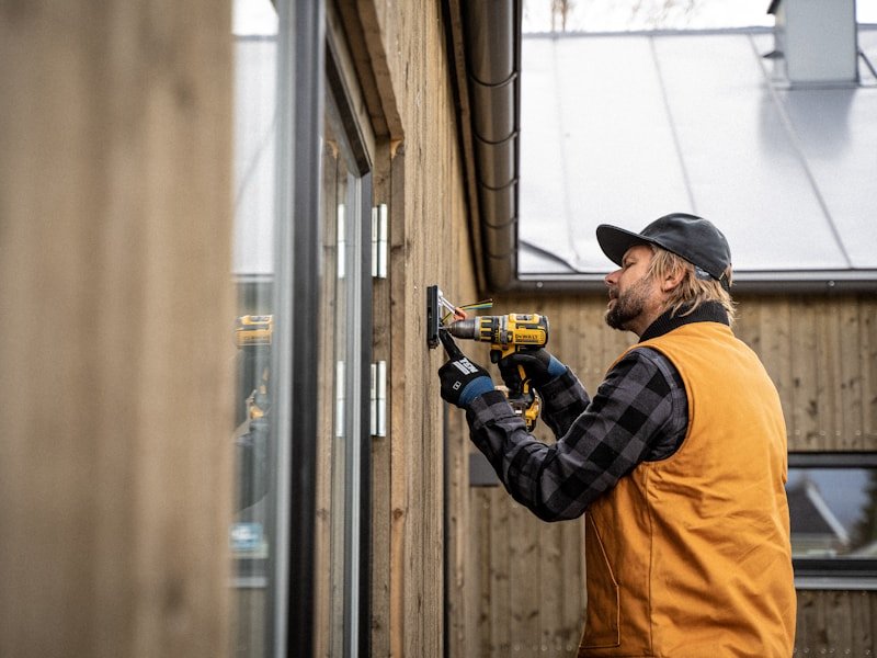 Handyman in plaid shirt and vest installing hardware on a home's wood exterior in winter.