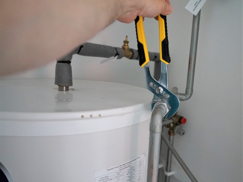 Hands tightening a fitting on a hot water tank with channel-lock pliers.