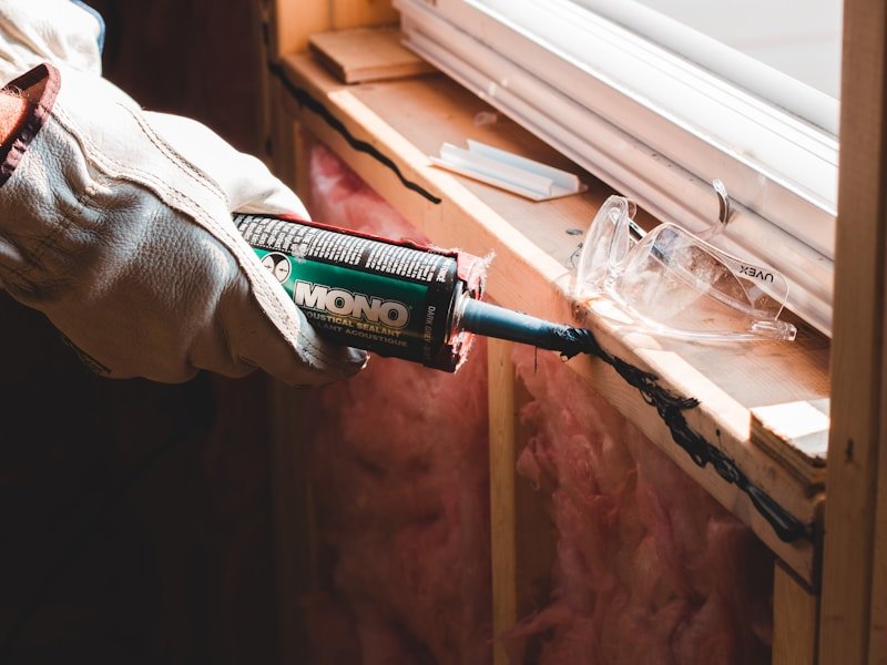 Gloved hand applying acoustical sealant to an insulated rim joist.